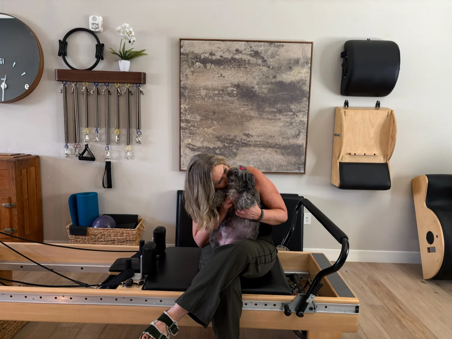 Patti sitting on the Reformer, embracing her dog